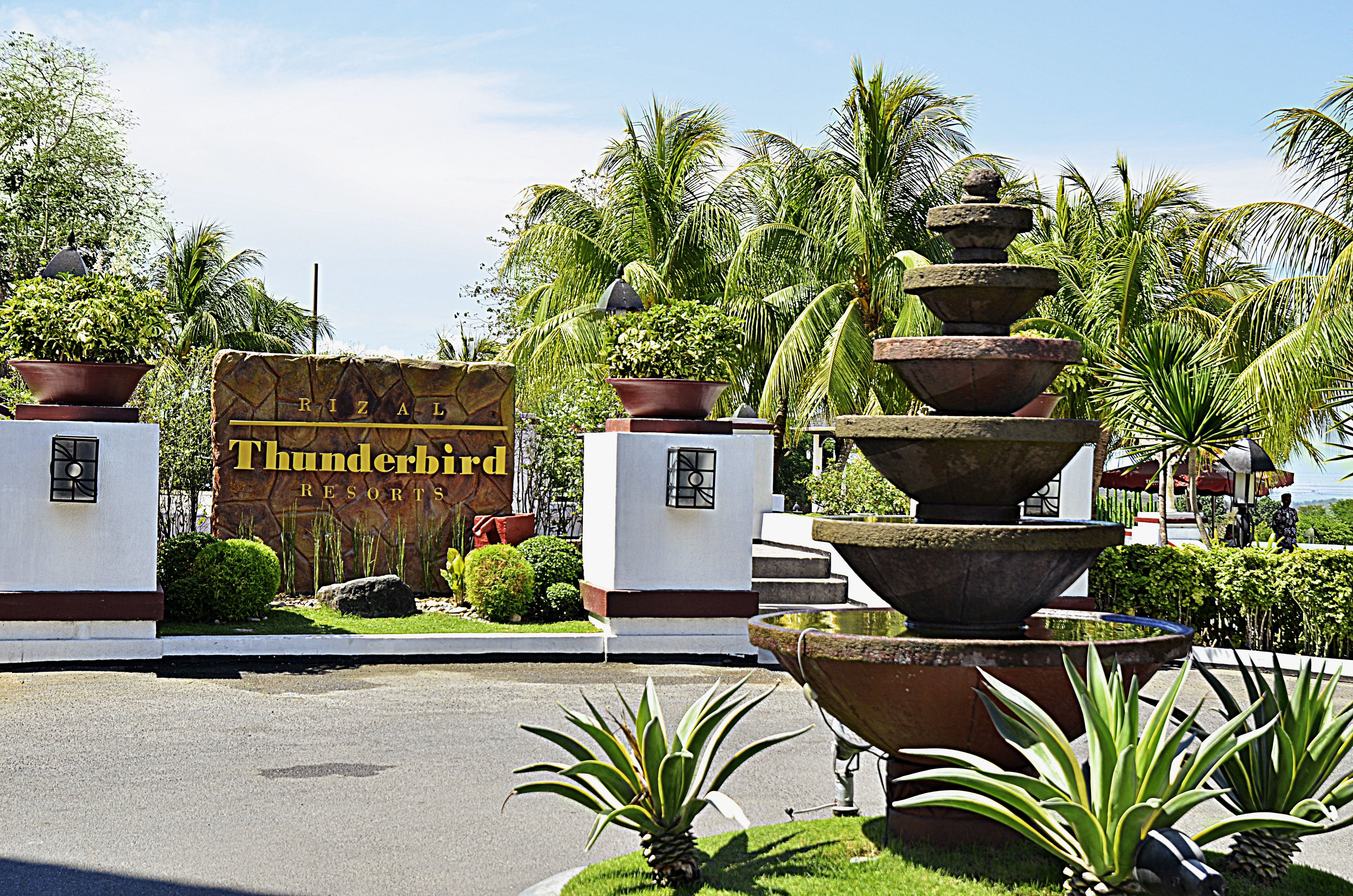 Señalización de 'Rizal Thunderbird Resorts' con una gran fuente y plantas tropicales.