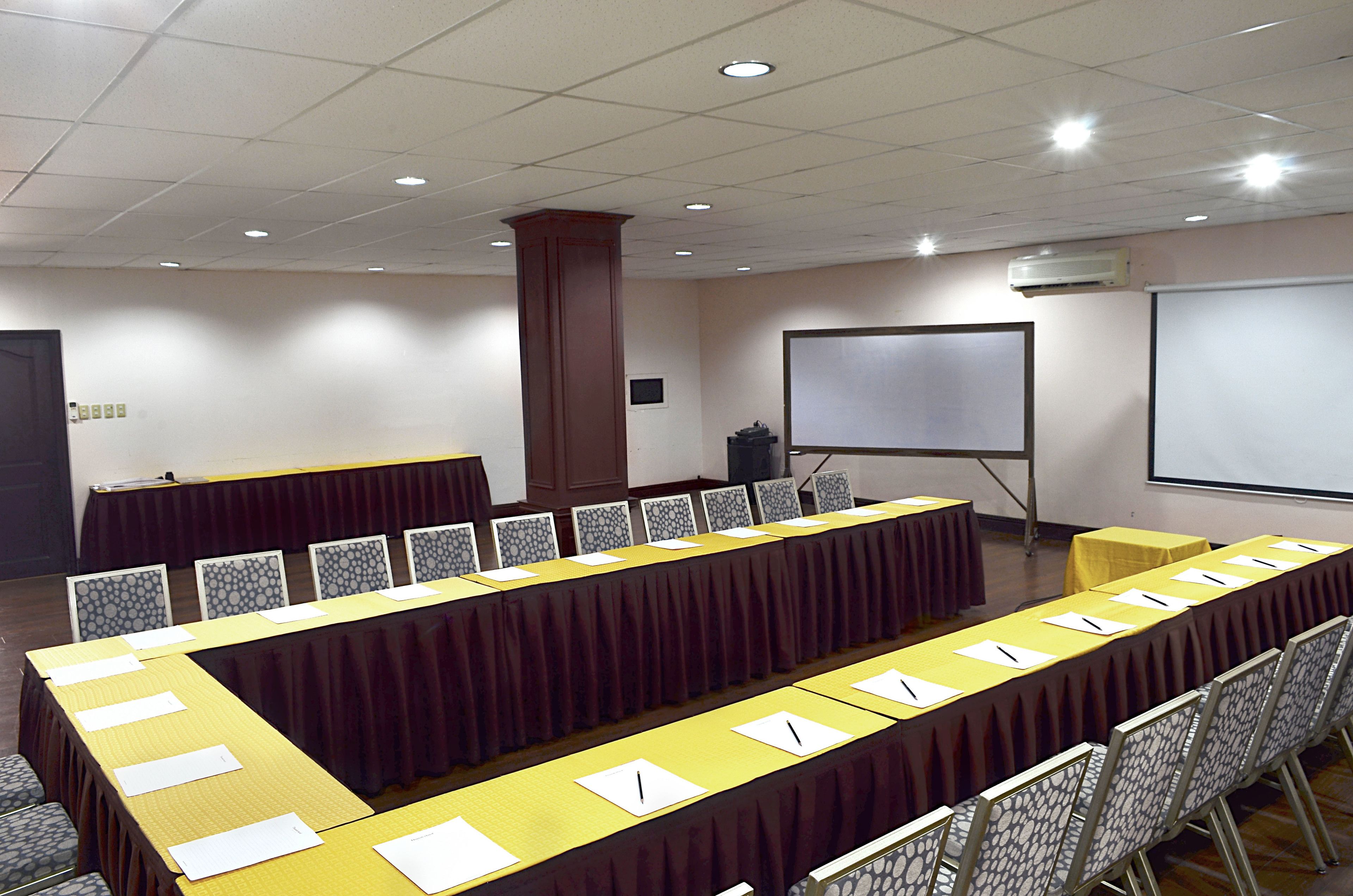 Una sala de conferencias con una larga mesa, sillas, una pantalla de proyector y un equipo de aire acondicionado.