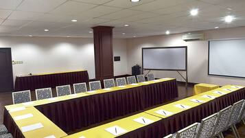 Una sala de conferencias con una larga mesa, sillas, una pantalla de proyector y un equipo de aire acondicionado.