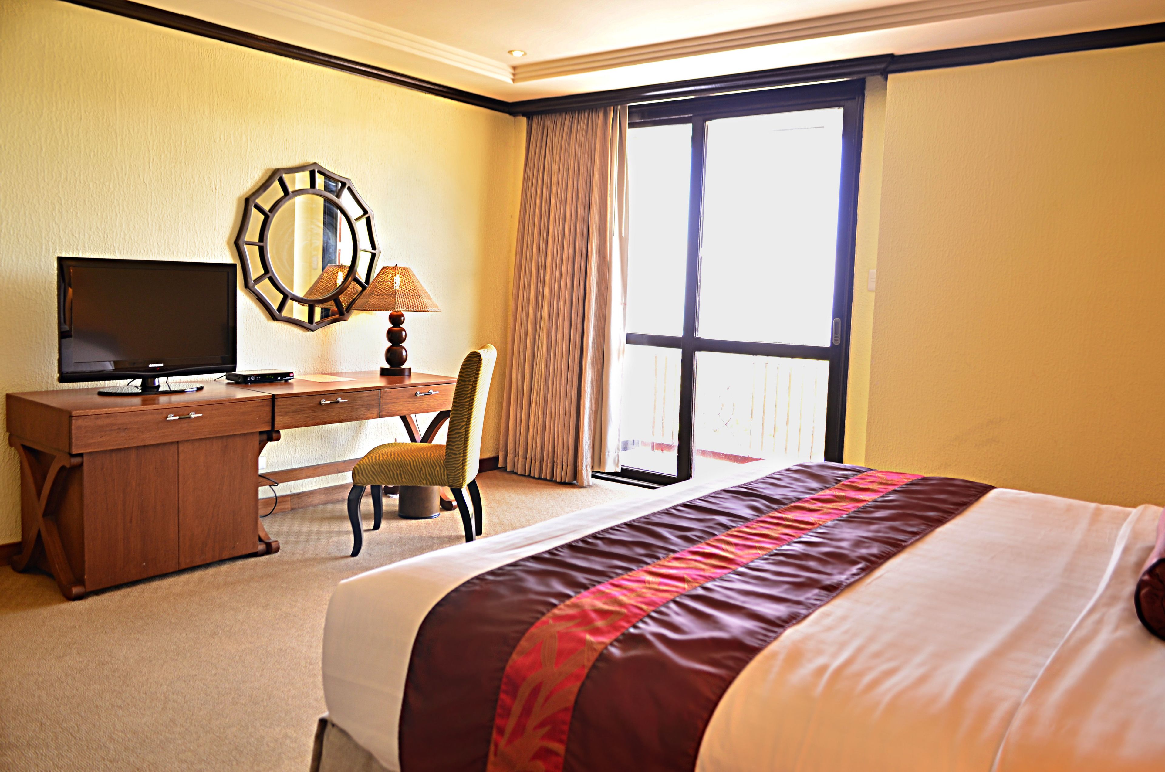 Hotelkamer met een groot bed, een bureau met een televisie, een stoel en een groot raam met gordijnen.