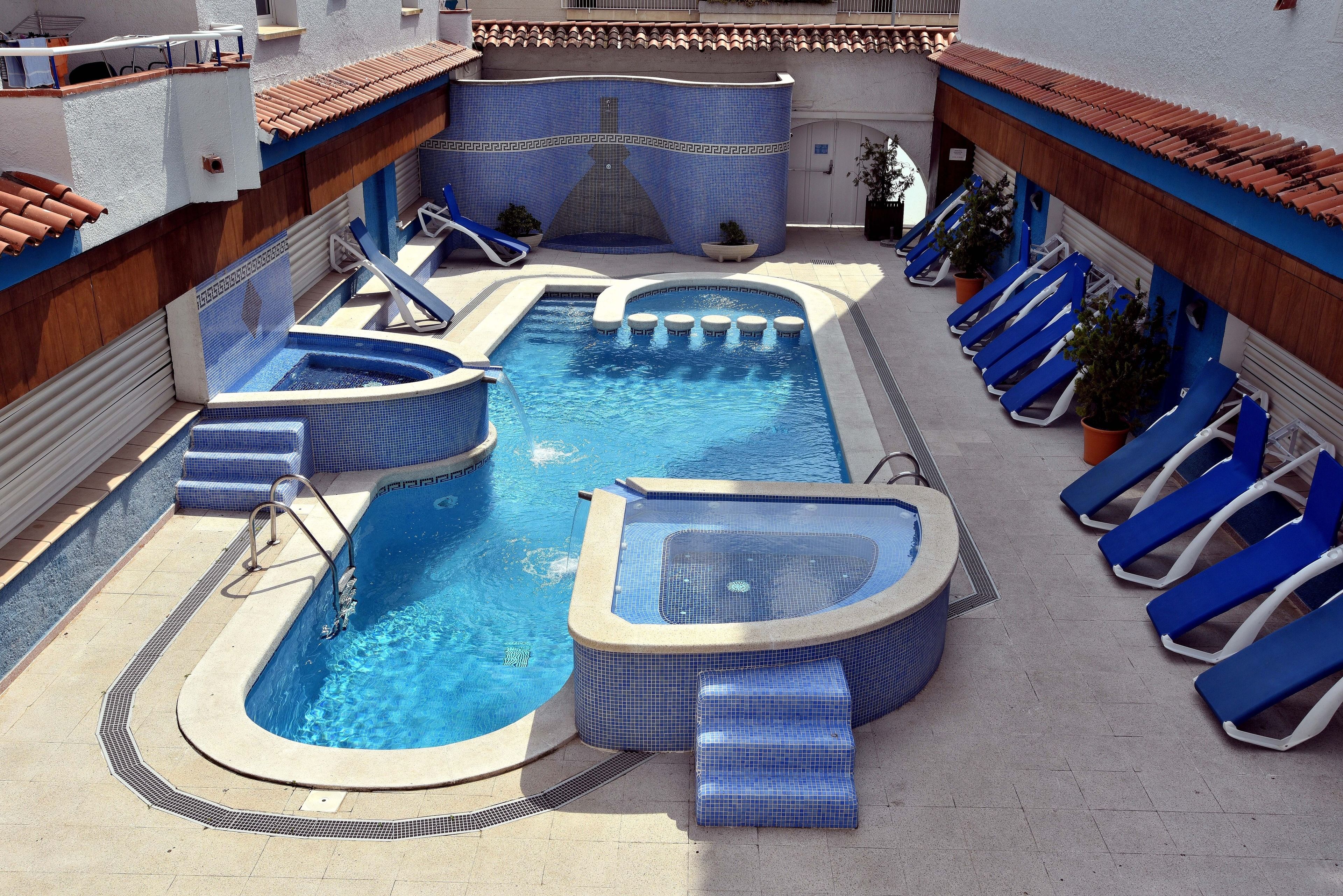 A swimming pool with multiple hot tubs and slides, surrounded by lounge chairs.