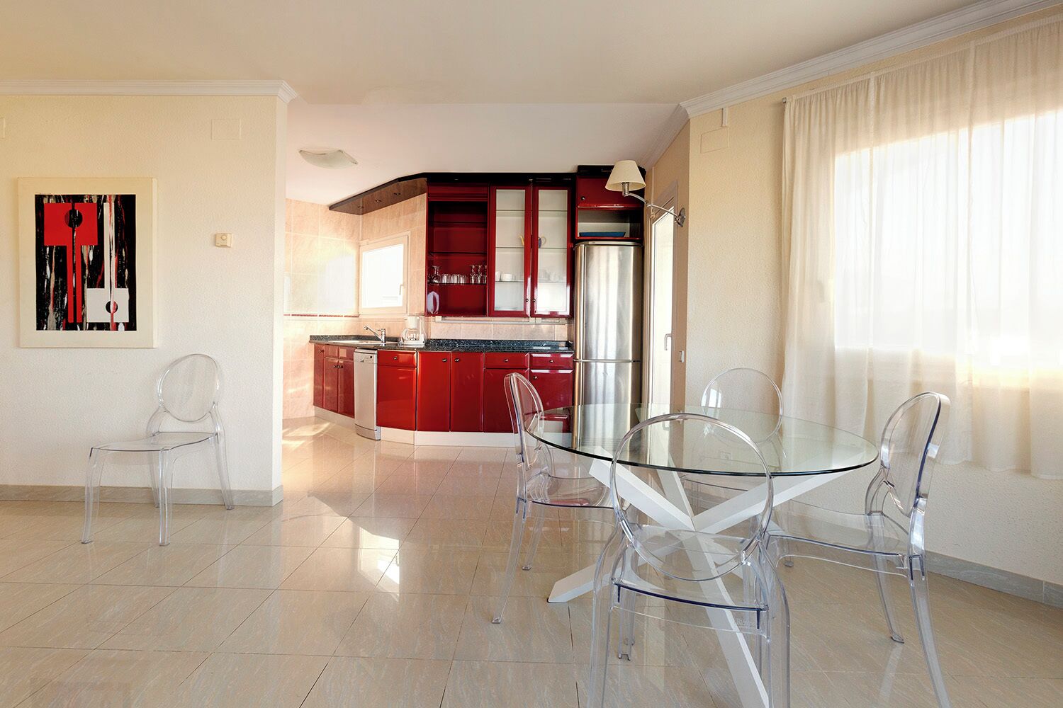 A modern kitchen with red cabinets and a glass dining table.