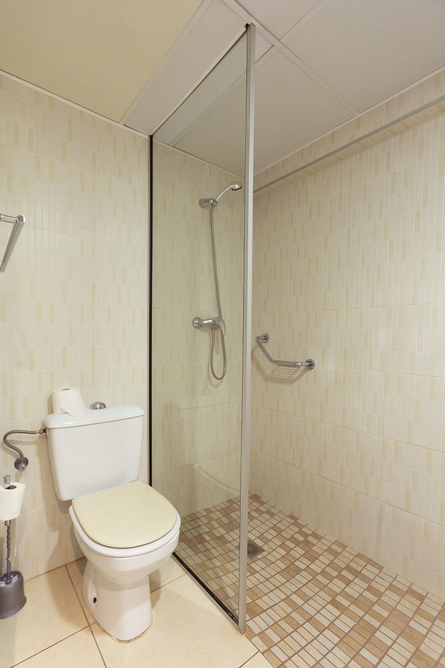 A bathroom with a toilet, a glass-enclosed shower, and tiled walls.