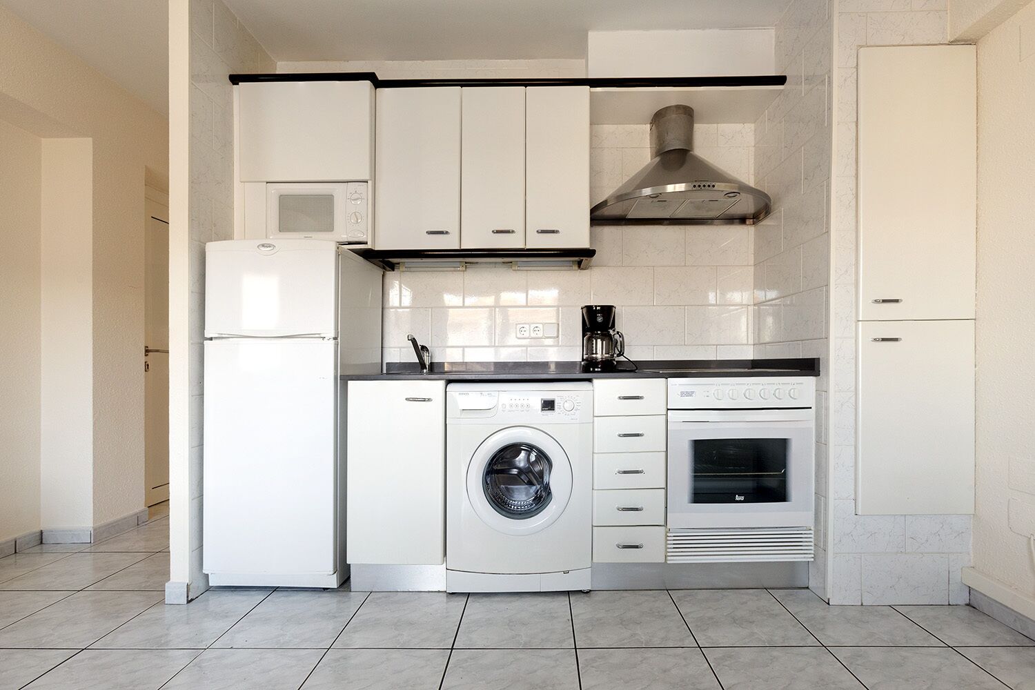 A compact kitchen with a washing machine, a coffee maker, and a built-in oven.
