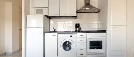 A compact kitchen with a washing machine, a coffee maker, and a built-in oven.