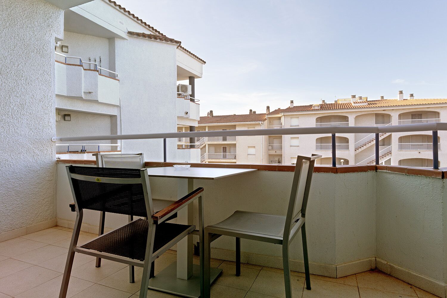 Ein Balkon mit zwei Stühlen und einem Tisch, mit Blick auf eine Reihe von Gebäuden mit Balkonen.