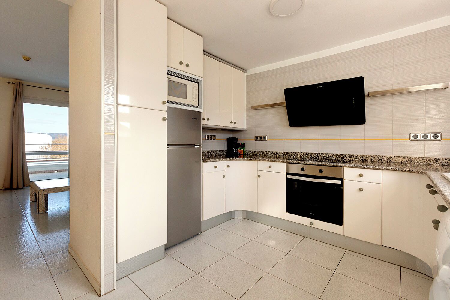 A modern kitchen with white cabinets, a built-in microwave, a stove, and a flat-screen TV mounted on the wall.