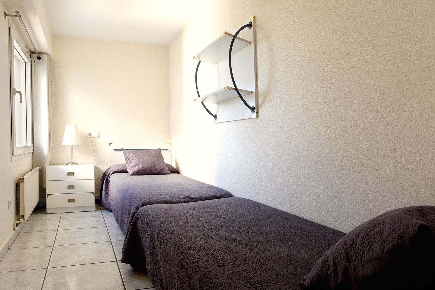 Een slaapkamer met twee bedden, een nachtkastje, een lamp en een wandplank.
