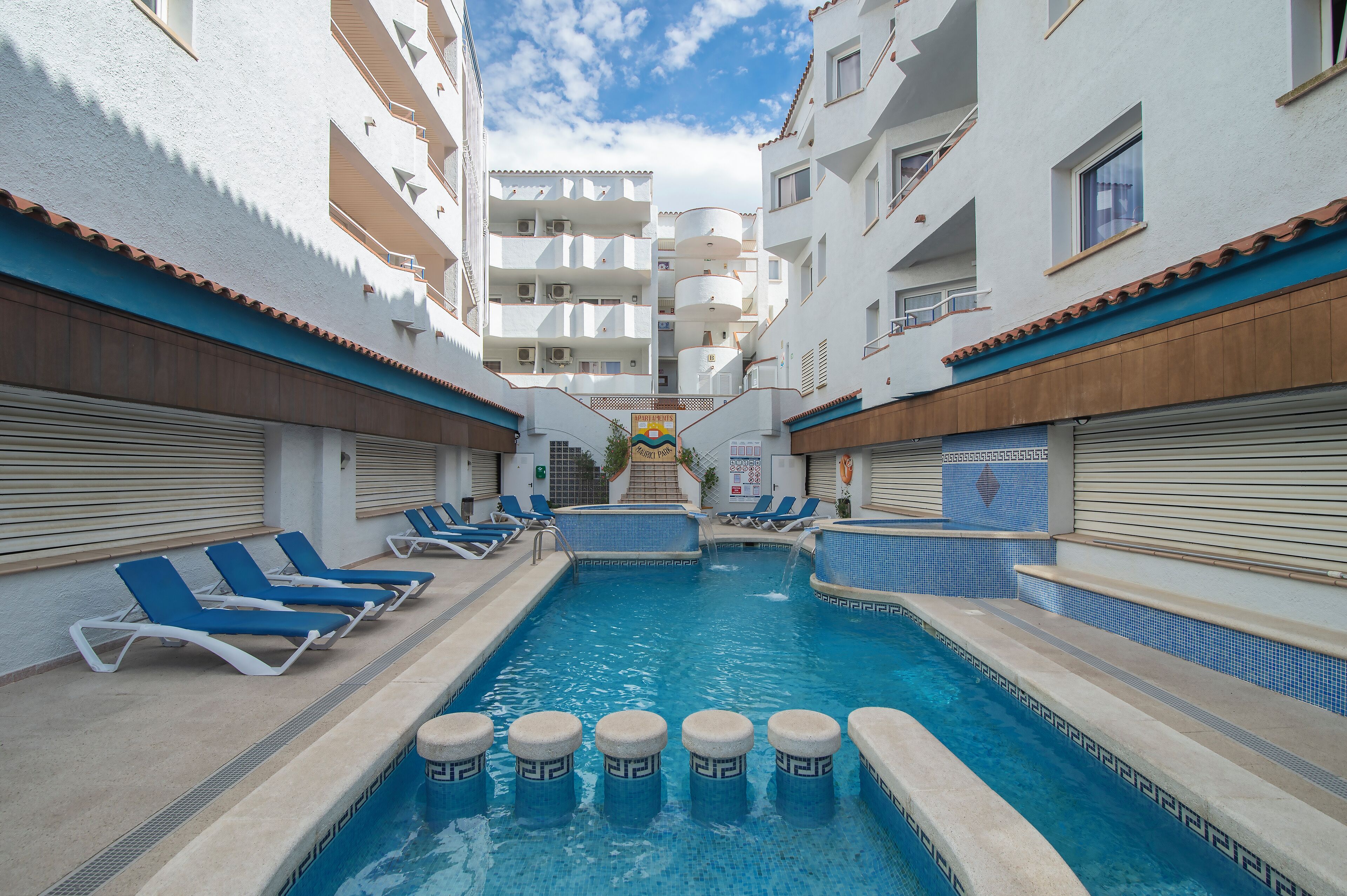 A swimming pool with blue lounge chairs and a small waterfall feature.