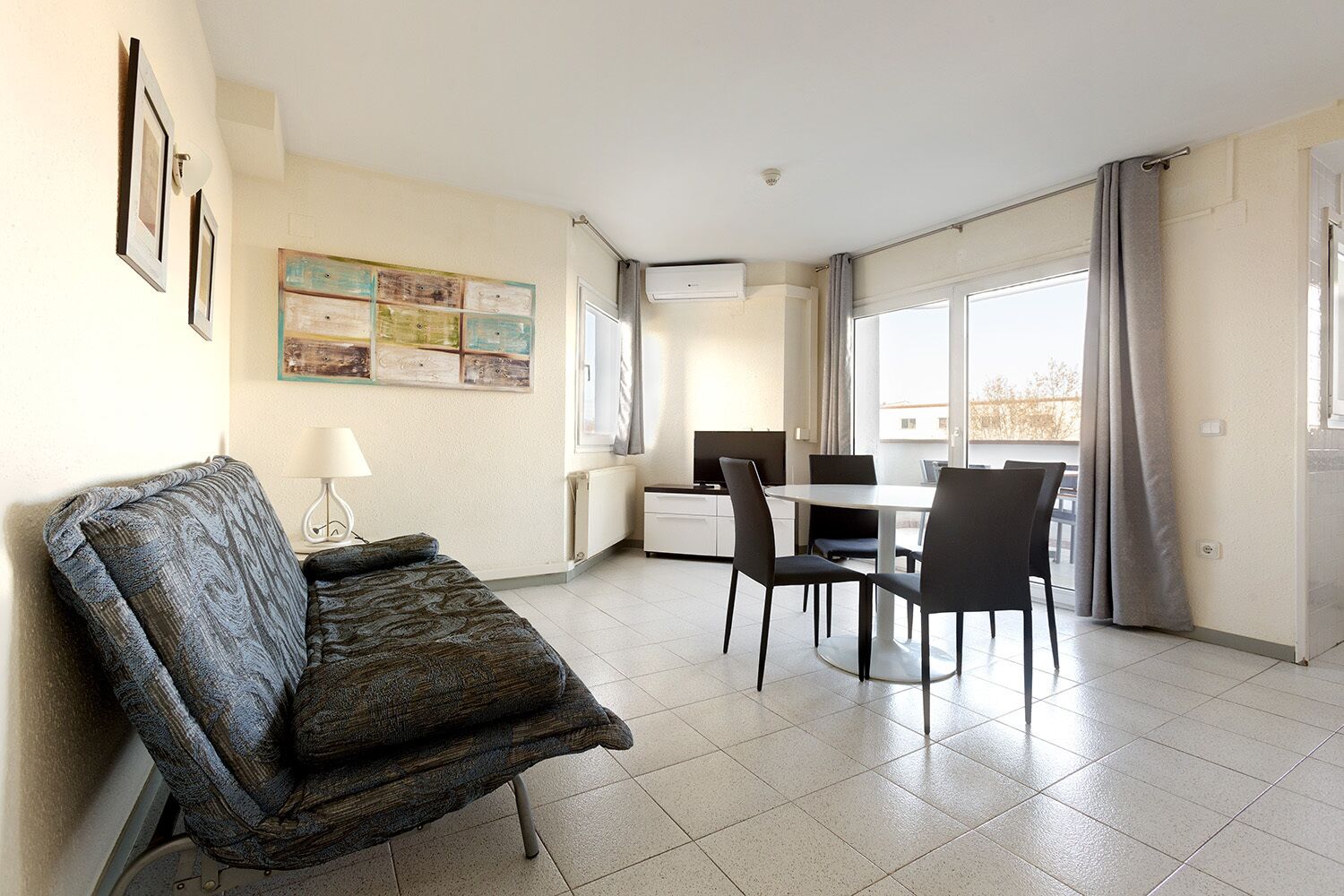 Una sala de estar moderna con un sofá, una mesa de comedor con sillas, un televisor y un ventanal con cortinas.