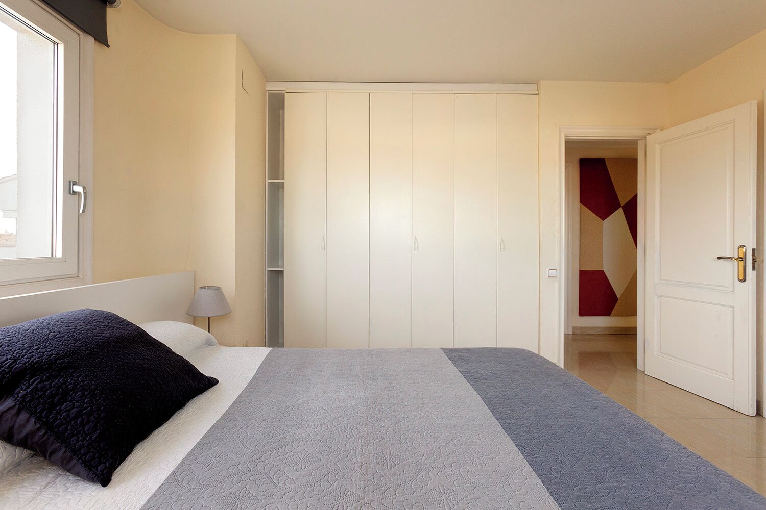 A bedroom with a bed, a wardrobe, a nightstand, and a lamp.