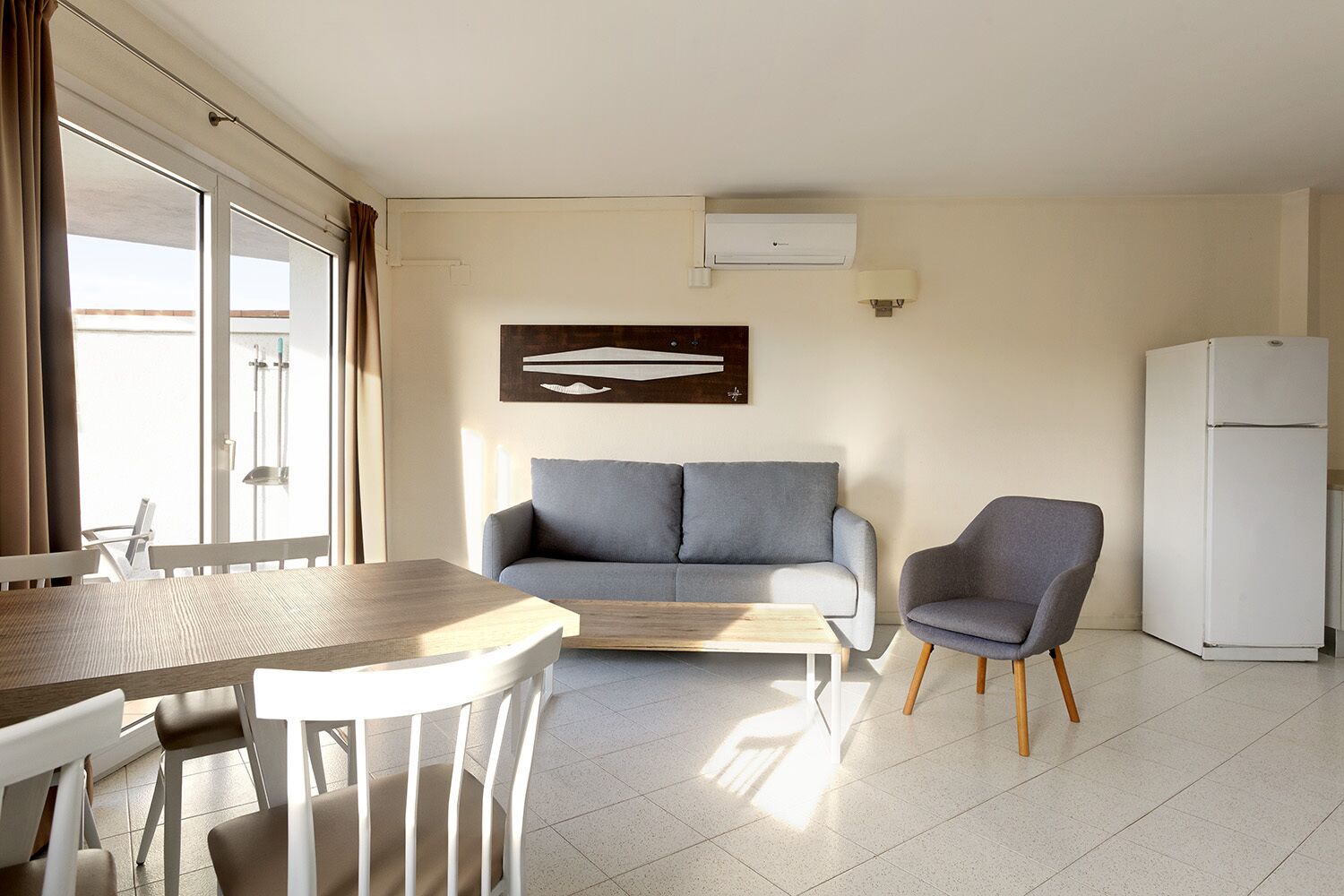 Una sala moderna con sofá, sillón, mesa de comedor y refrigerador.