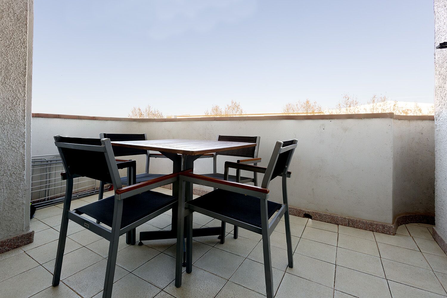 Een klein terras buiten met een tafel en vier stoelen.