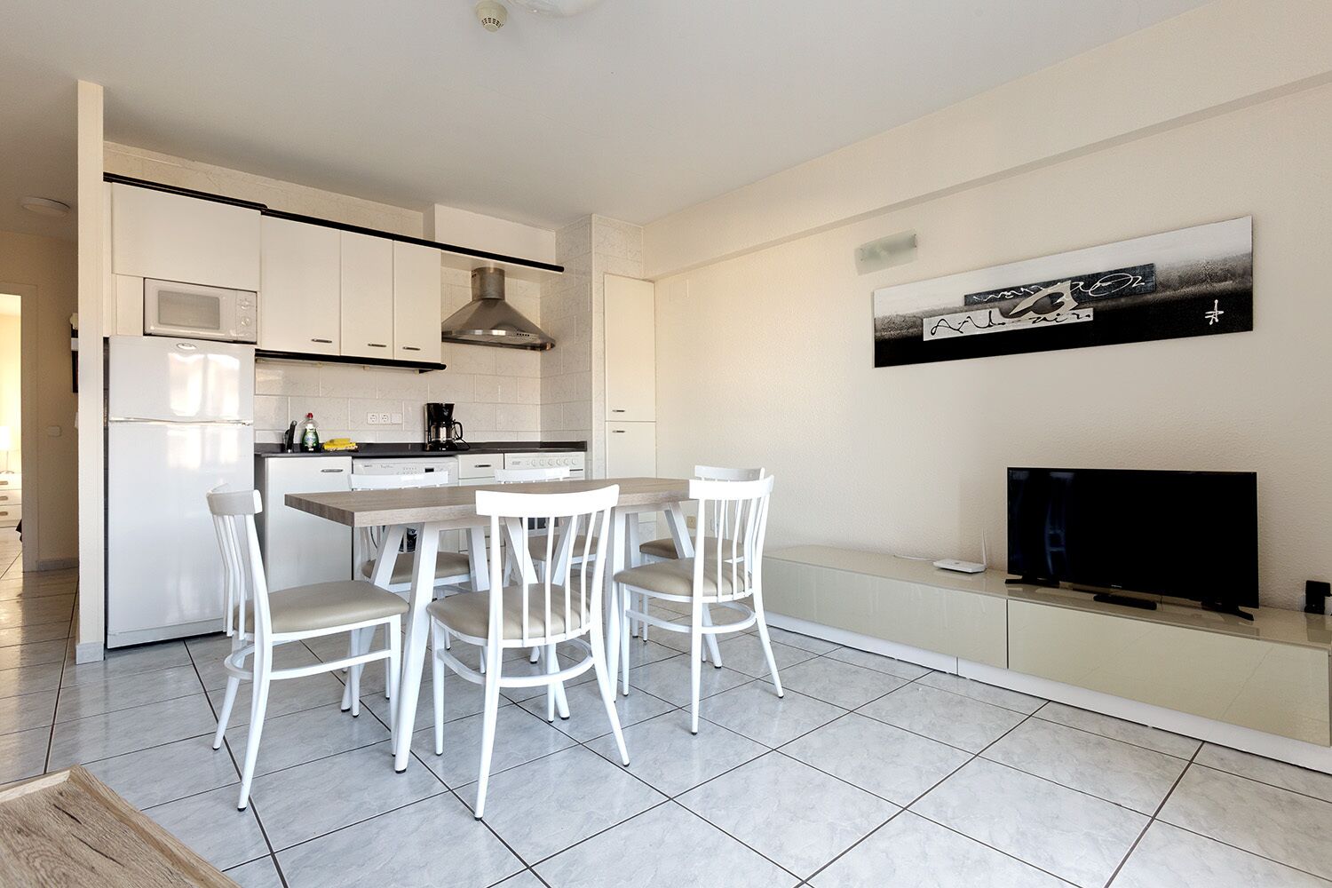 A modern kitchen with white cabinetry, a central island, and a dining area with white chairs.