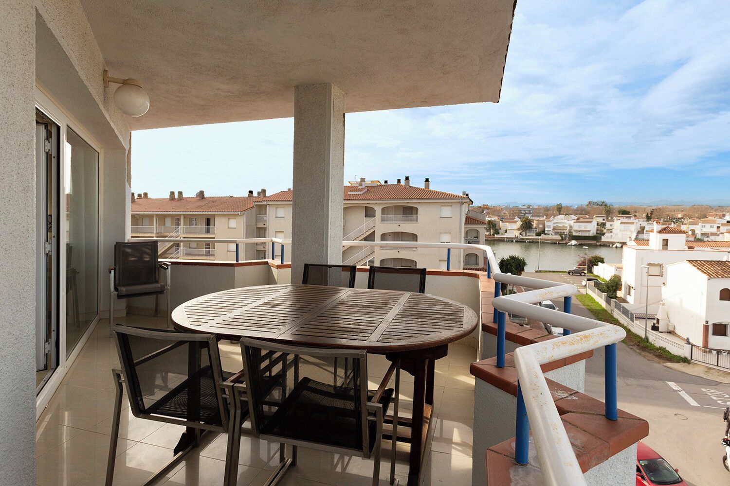 Un balcon avec une table ronde et des chaises, donnant sur un quartier résidentiel avec une rivière et des immeubles.