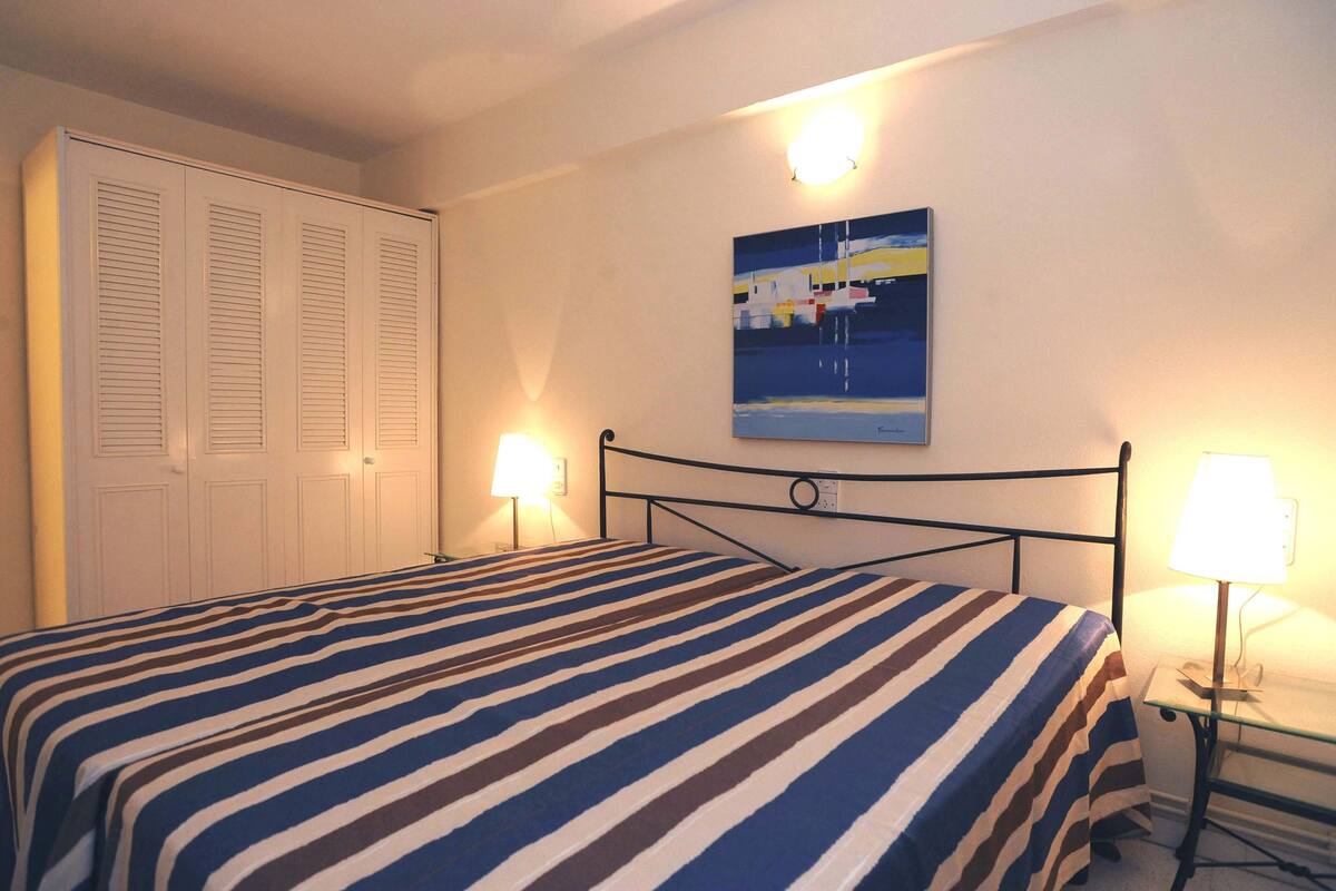Een slaapkamer met een bed, nachtlampjes, een schilderij aan de muur en een kledingkast.