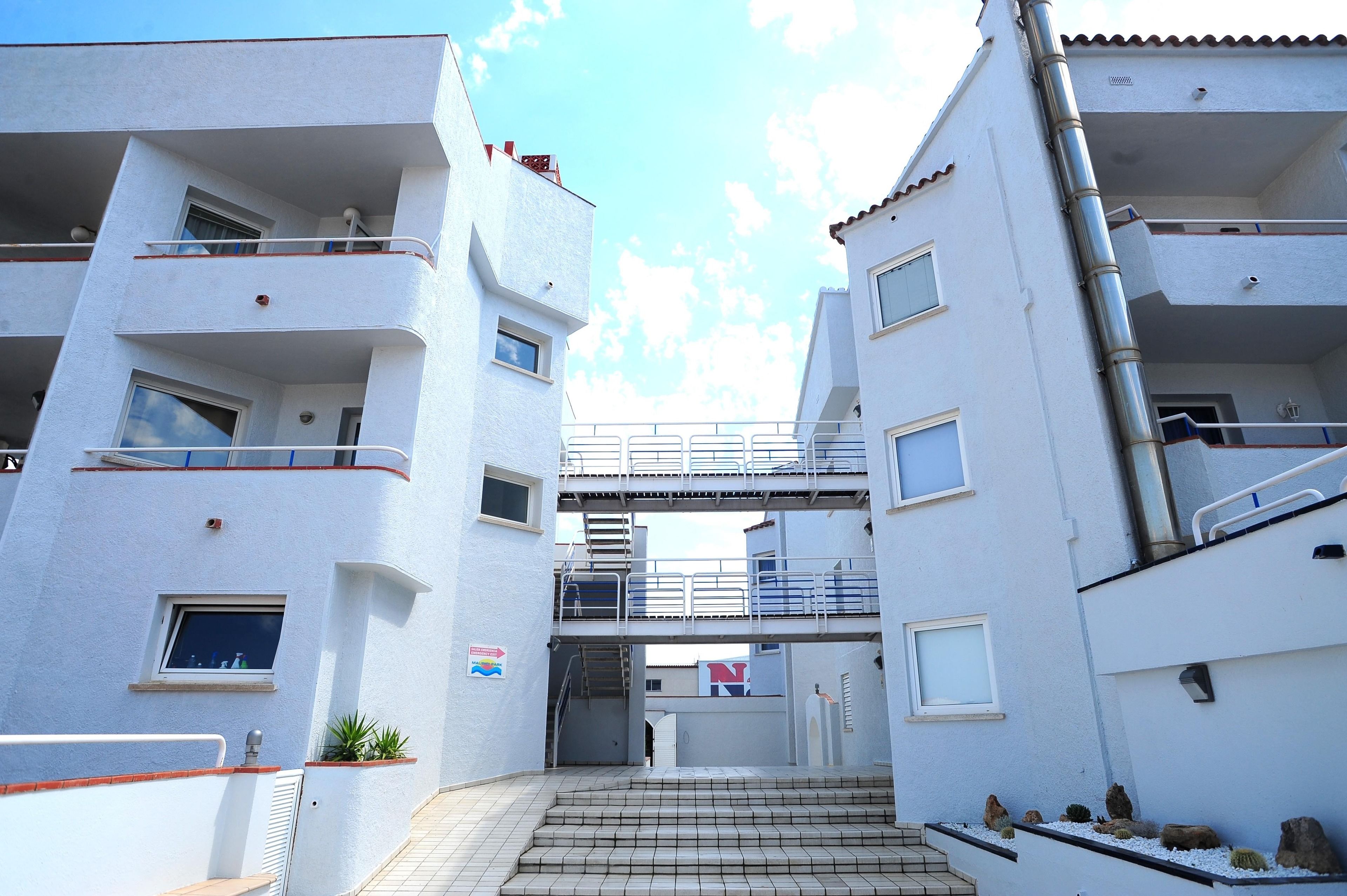 Un immeuble résidentiel à plusieurs étages, doté de balcons, d’un escalier central et surplombant un ciel dégagé.