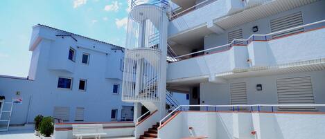 Un edificio de varios pisos con una escalera espiral central, asientos exteriores y un cielo despejado.