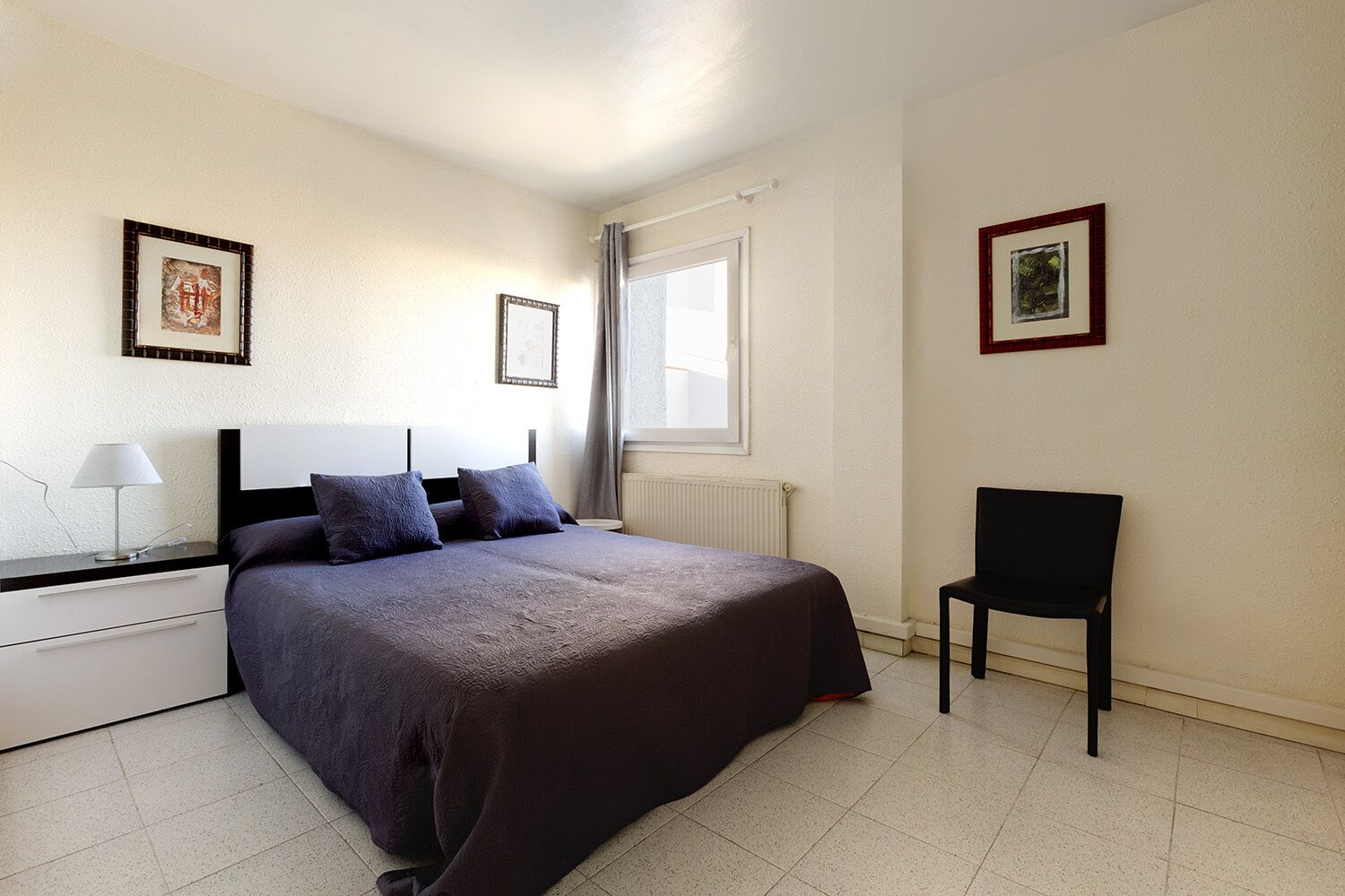 Une chambre à coucher comprenant un lit, une chaise, une table de chevet, une lampe et deux tableaux encadrés accrochés au mur.