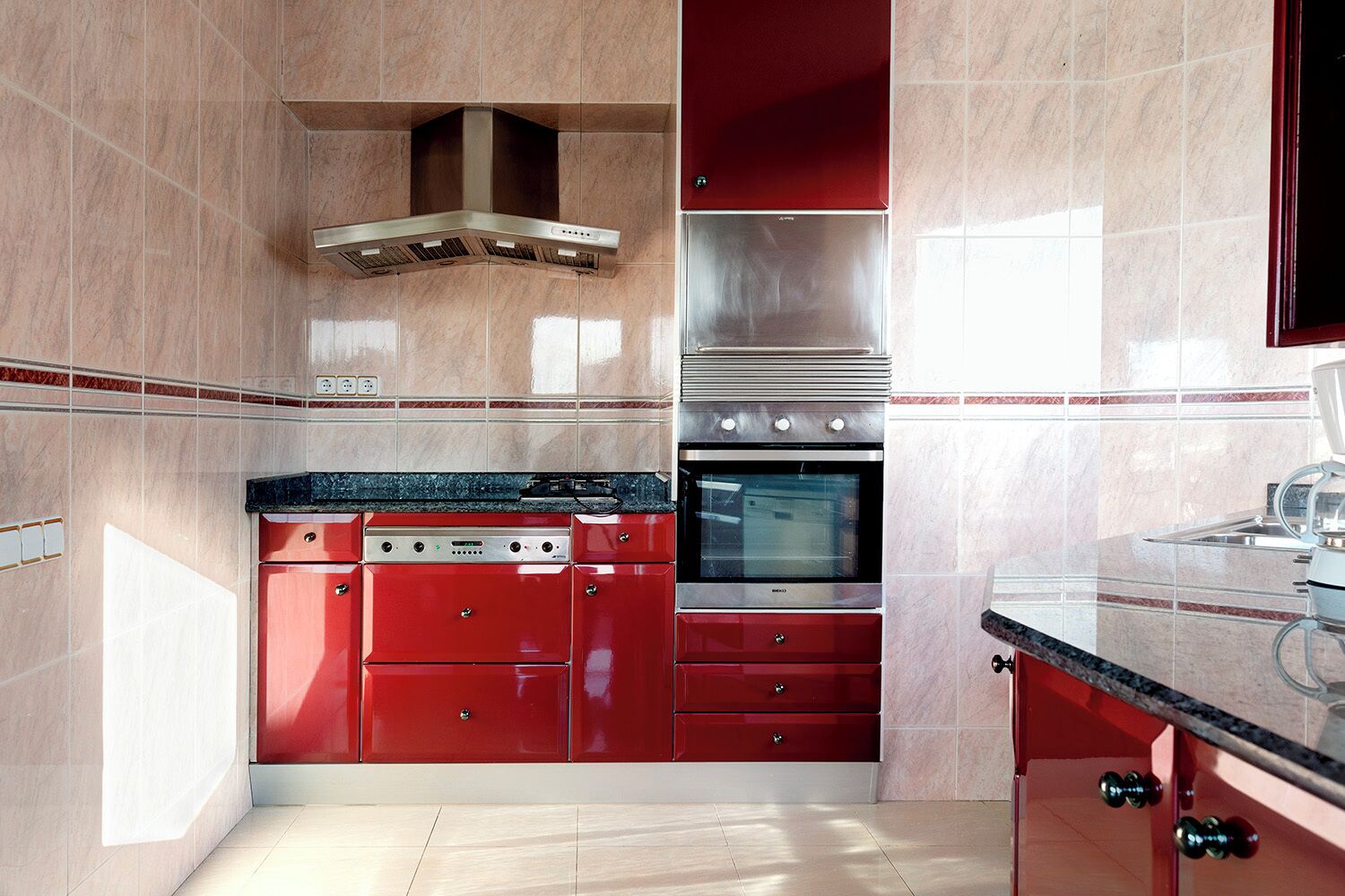 Une cuisine moderne avec des meubles de rangement rouges, une hotte de cuisine en acier inoxydable, un four et un micro-ondes encastré.