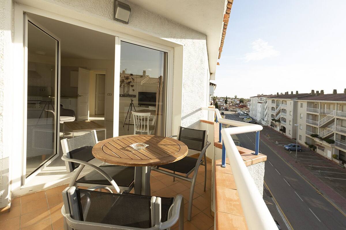 Een balkon met een tafel en stoelen, een schuifdeur naar een binnenruimte en uitzicht op een woonstraat.