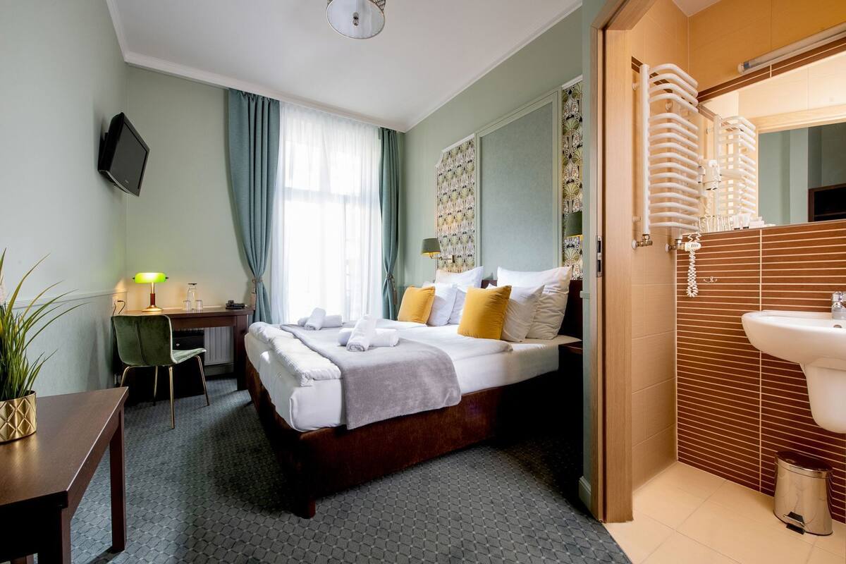 Une chambre d’hôtel comprenant un lit, une table de chevet, une lampe, une télévision et une salle de bain avec un lavabo et un miroir.