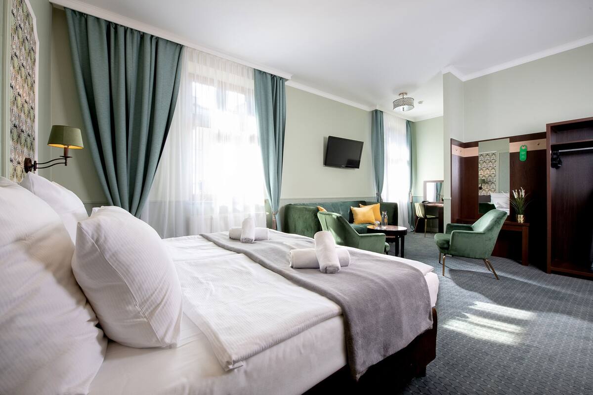Une chambre d’hôtel avec un lit, un fauteuil vert, une petite table et un téléviseur fixé au mur.