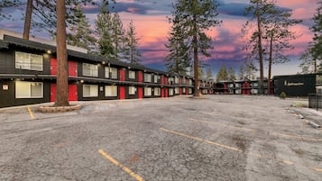 A row of motel buildings with a parking lot in front, surrounded by trees and a sunset sky.