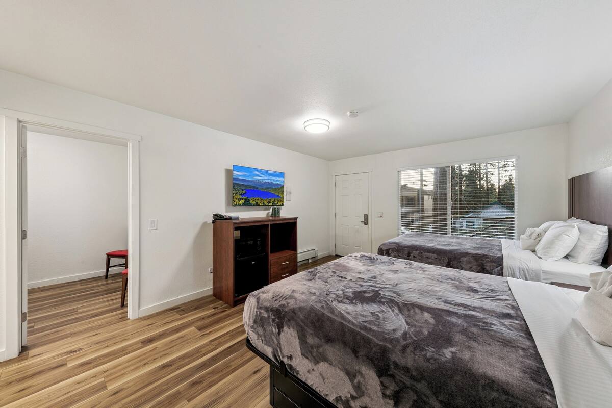 Een slaapkamer met twee bedden, een houten vloer, een televisie op een standaard en een raam met jaloezieën.