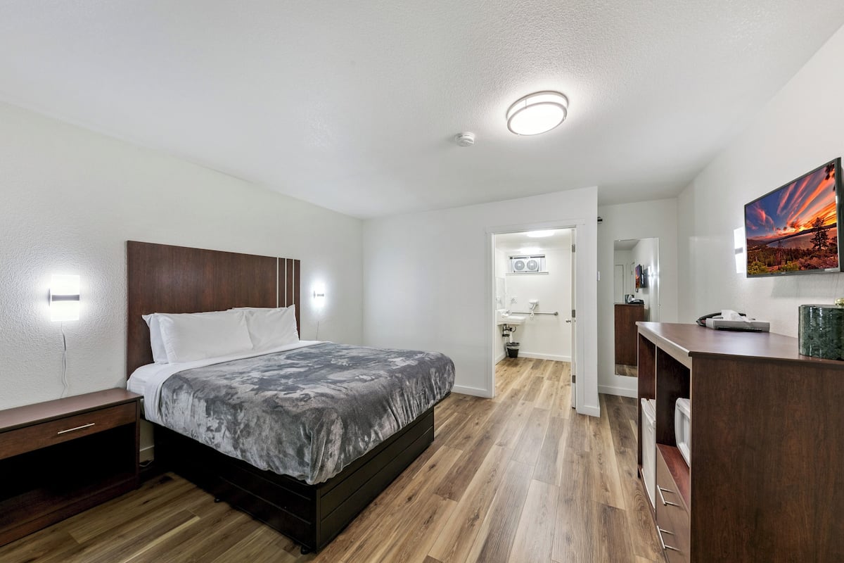 Een slaapkamer met een bed, nachtkastjes, een bureau en een badkamer zichtbaar door een geopende deur.