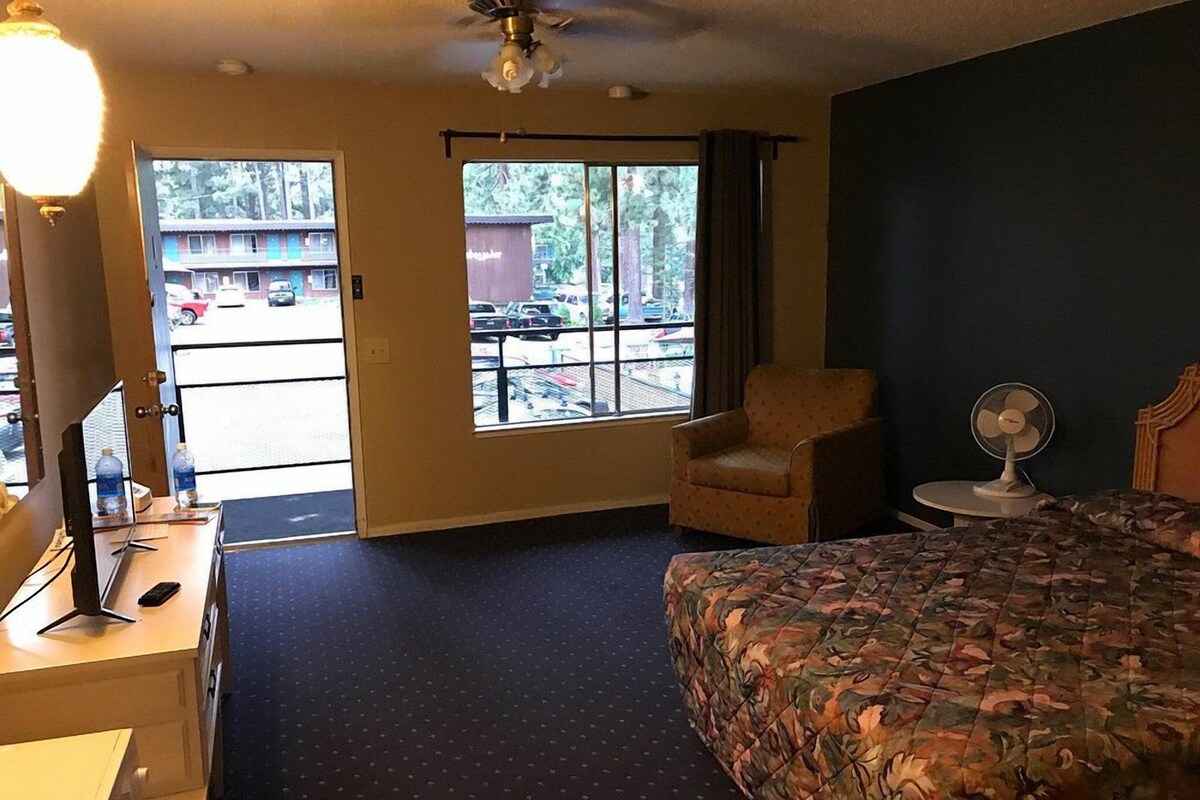 Habitación de hotel con una cama, un escritorio con computadora, una silla, una ventana que da a un estacionamiento y un ventilador de techo.