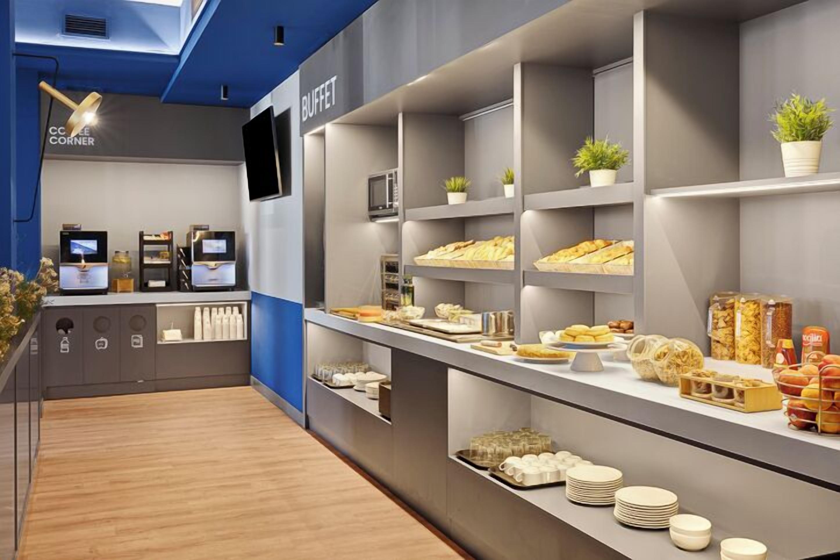 A buffet area with multiple shelves displaying food items, a coffee station, and a television screen.