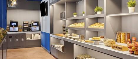 Uma área de buffet com várias prateleiras exibindo alimentos, um canto para café e uma tela de televisão.