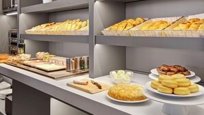 Un buffet proposant une variété de produits de boulangerie, notamment des pâtisseries et du pain, présentés sur des étagères et dans des assiettes.