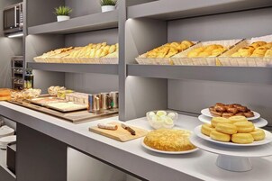 Un bufé con diversas opciones de panadería, incluyendo pasteles y pan, dispuesto en estantes y platos.