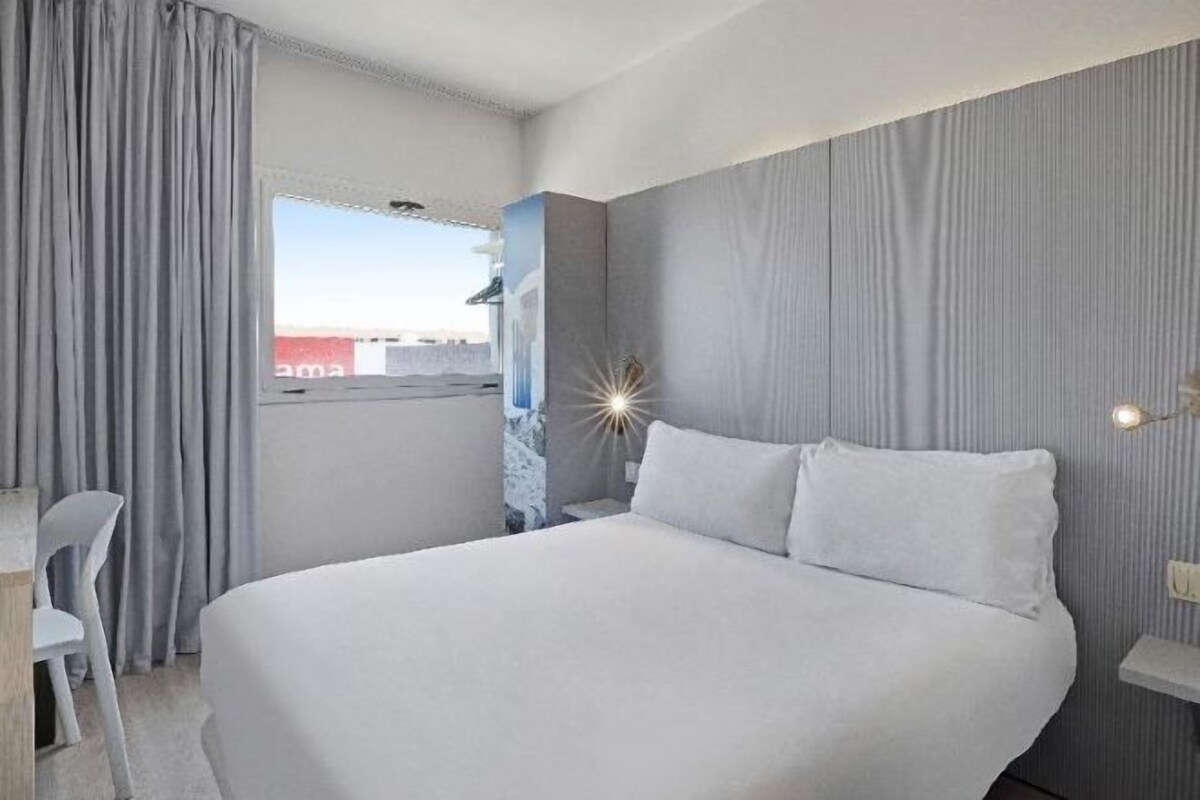 Ein Hotelzimmer mit einem großen Bett, einem Schreibtisch und einem Fenster mit Vorhängen.