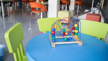 Zona de juegos infantiles con una mesa azul y sillas de colores.