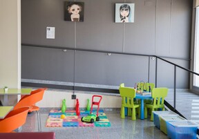 Un área de juegos infantiles con sillas coloridas, una mesita y juguetes sobre una alfombra.