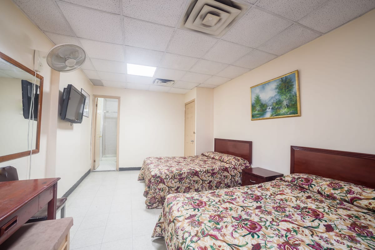 A hotel room with two beds, a desk, a chair, a TV, a painting, and a door leading to another room.