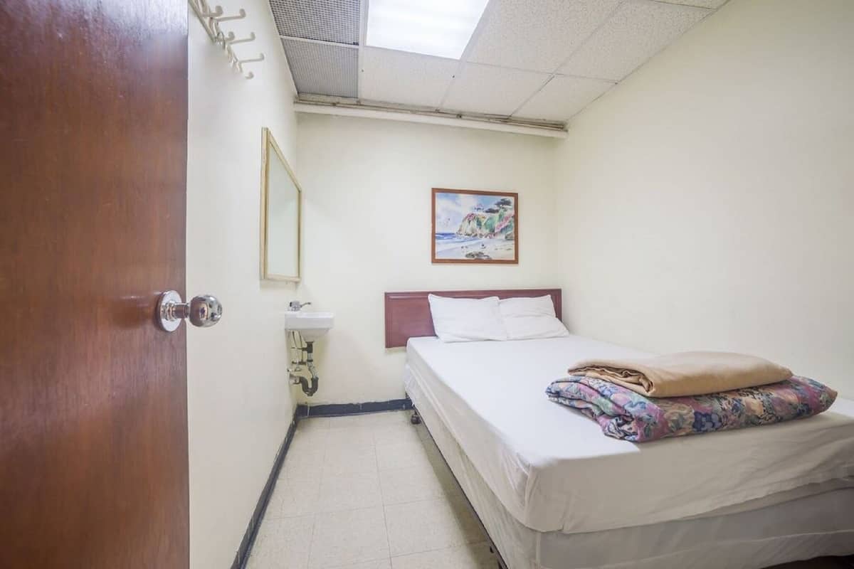 A hotel room with a bed, a bedside table, a mirror, and a painting on the wall.