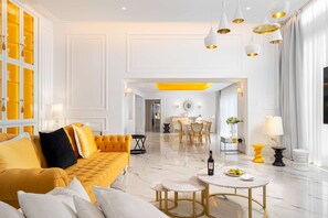 A spacious living area with a yellow sofa, a round table, and a chandelier.
