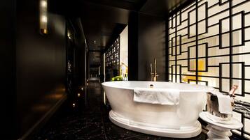 A luxurious bathroom with a freestanding bathtub, a decorative wall panel, and a champagne bucket on a pedestal.