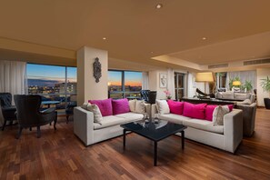 A spacious living room with a large window offering a city view, a black coffee table, and two sofas with colorful cushions.