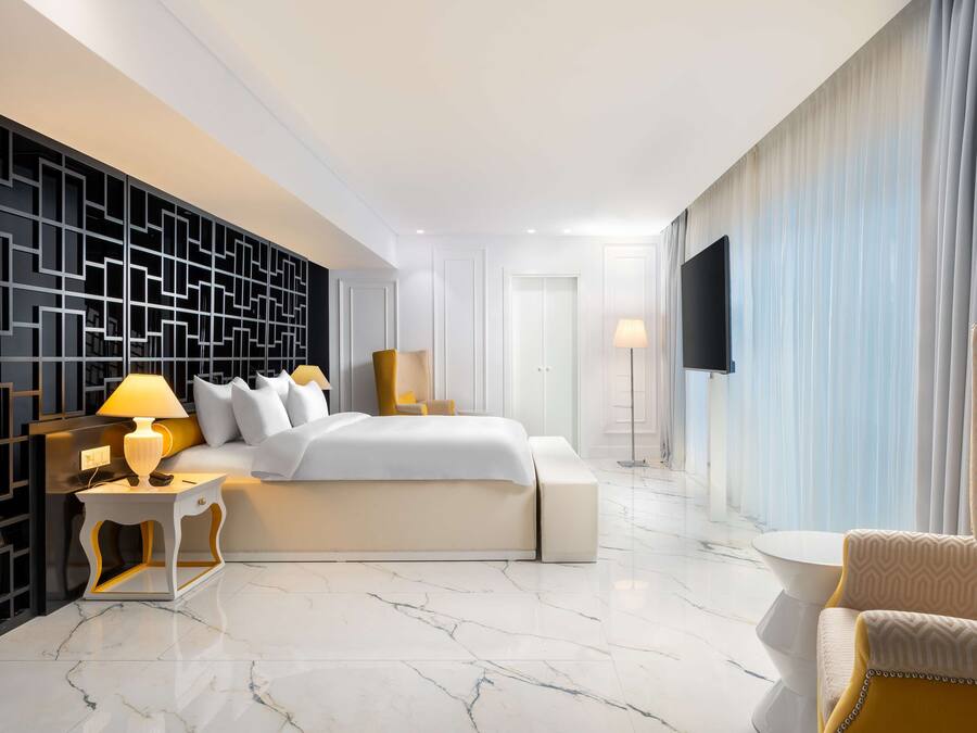 Una habitación de hotel moderna con una cama grande, un área de descanso con una silla, un televisor y un panel decorativo en la pared.