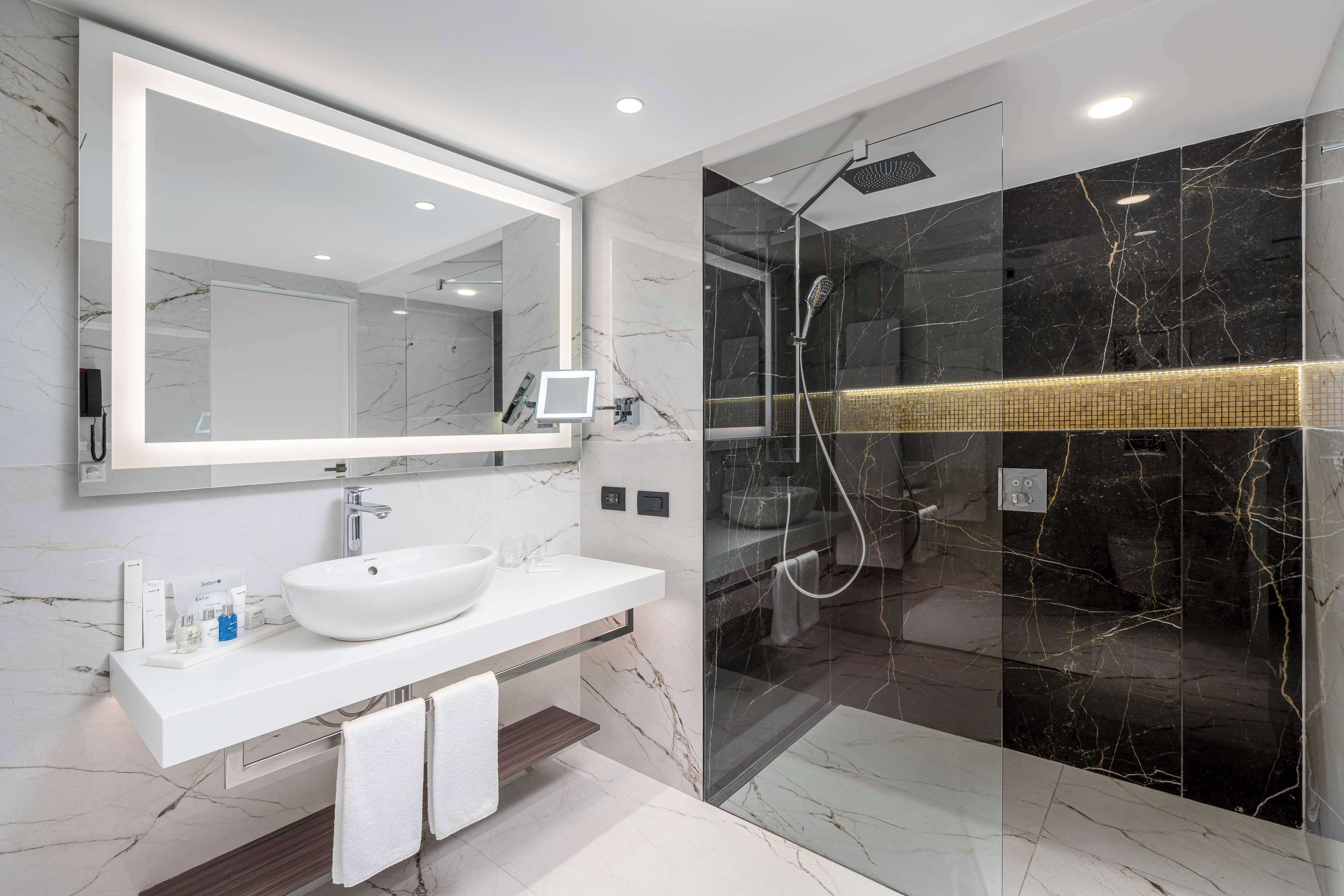 A modern bathroom with a white sink, large mirror, and a glass-enclosed shower area.