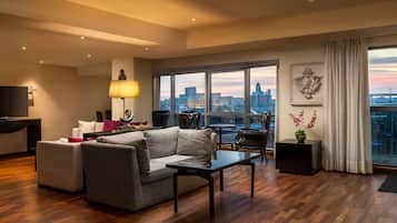 A spacious living room with a large window offering a city view, a sofa, a coffee table, and a TV on a stand.