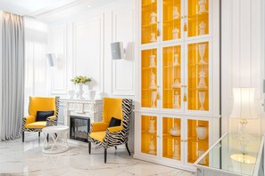 A room with two zebra-striped armchairs, a white fireplace, and a glass cabinet with yellow doors displaying white vases.