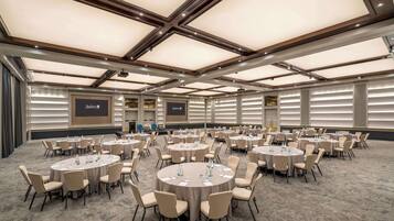 Un salón de conferencias amplio con varias mesas redondas y sillas, un techo alto con diseño de cuadrícula y suelo alfombrado.