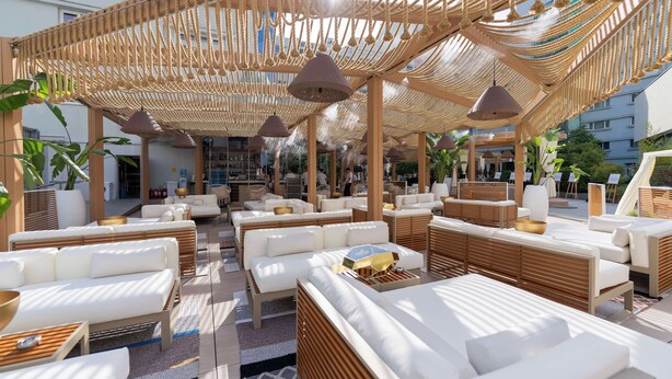 Un área de lounge en la azotea con diversas opciones de asientos, incluyendo sofás y sillones, bajo un toldo tejido.