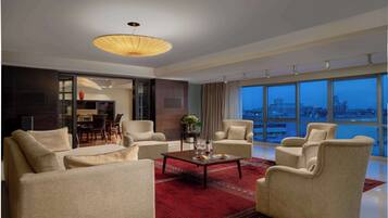 A modern living room with a large window, a red rug, and a dining area visible through an open door.